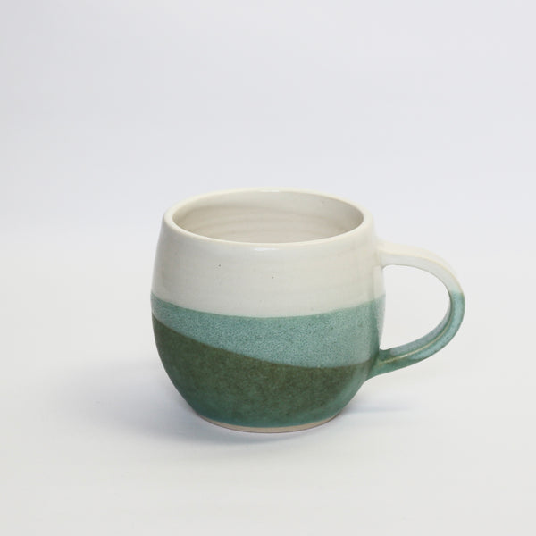 stoneware curved mug, glazed in white and dark bluey, green. the overlap is a mid green