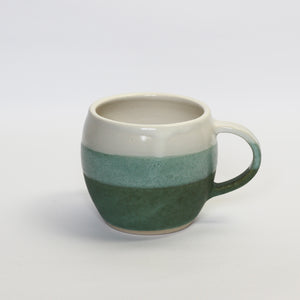 stoneware curved mug, glazed in white and dark bluey, green. the overlap is a mid green