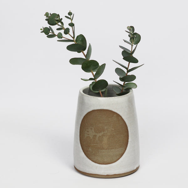 toasted stoneware vase, glazed in white with large unglazed circle, holding a eucalyptus branch